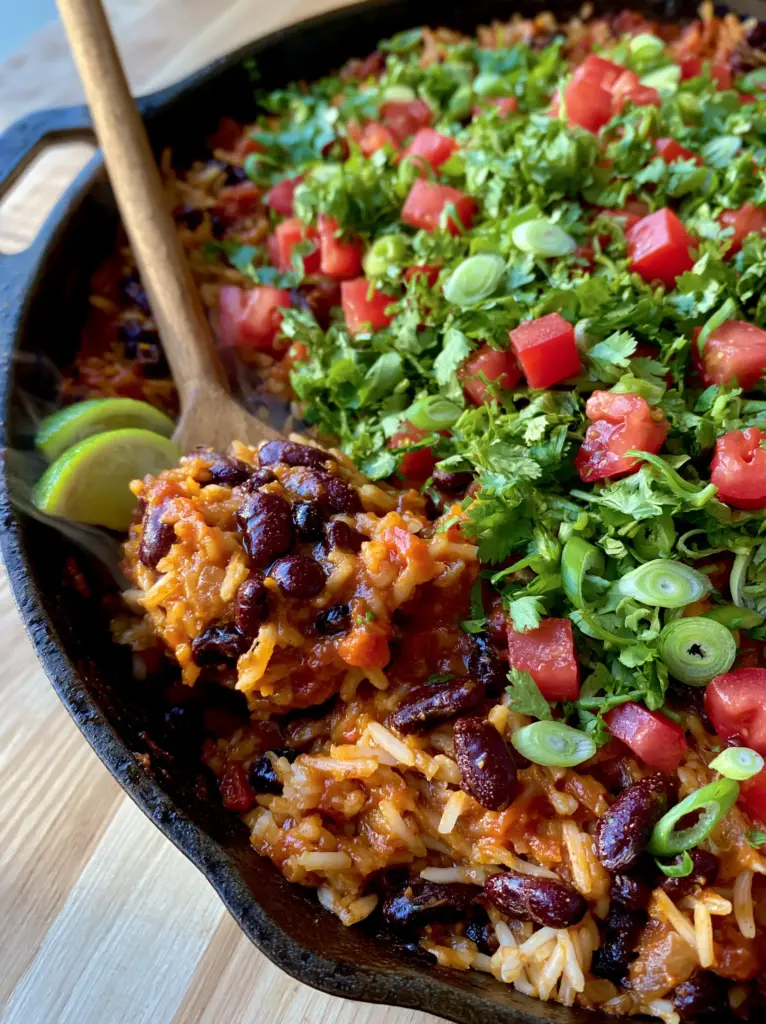 A wooden spoon lifting a scoop of Kidney Beans and Rice Skillet from a cast iron pan, revealing steam and saucy consistency.