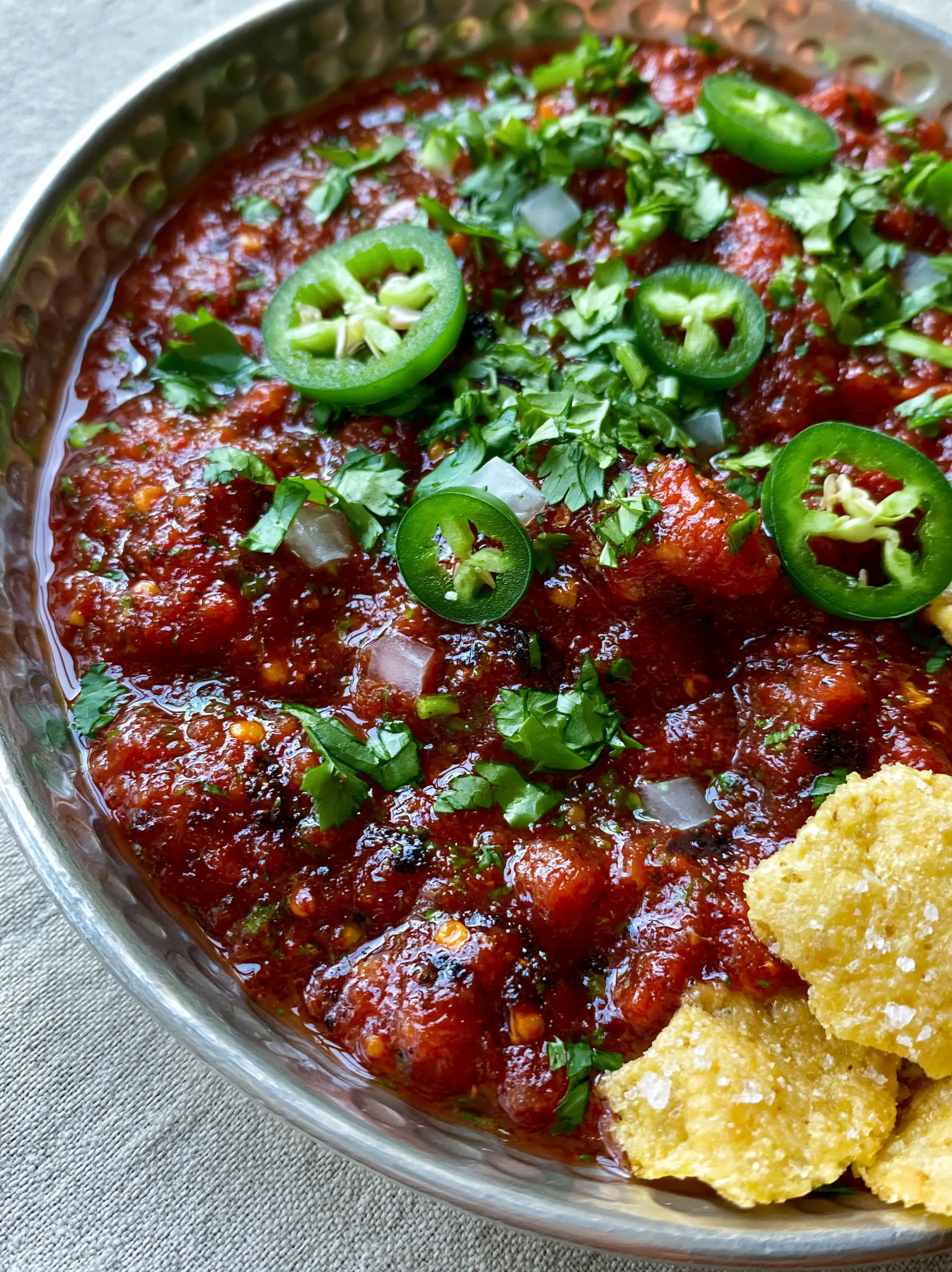Close up of Blender salsa showing fire-roasted tomato char flecks, cilantro, and sliced jalapeños with seeds.