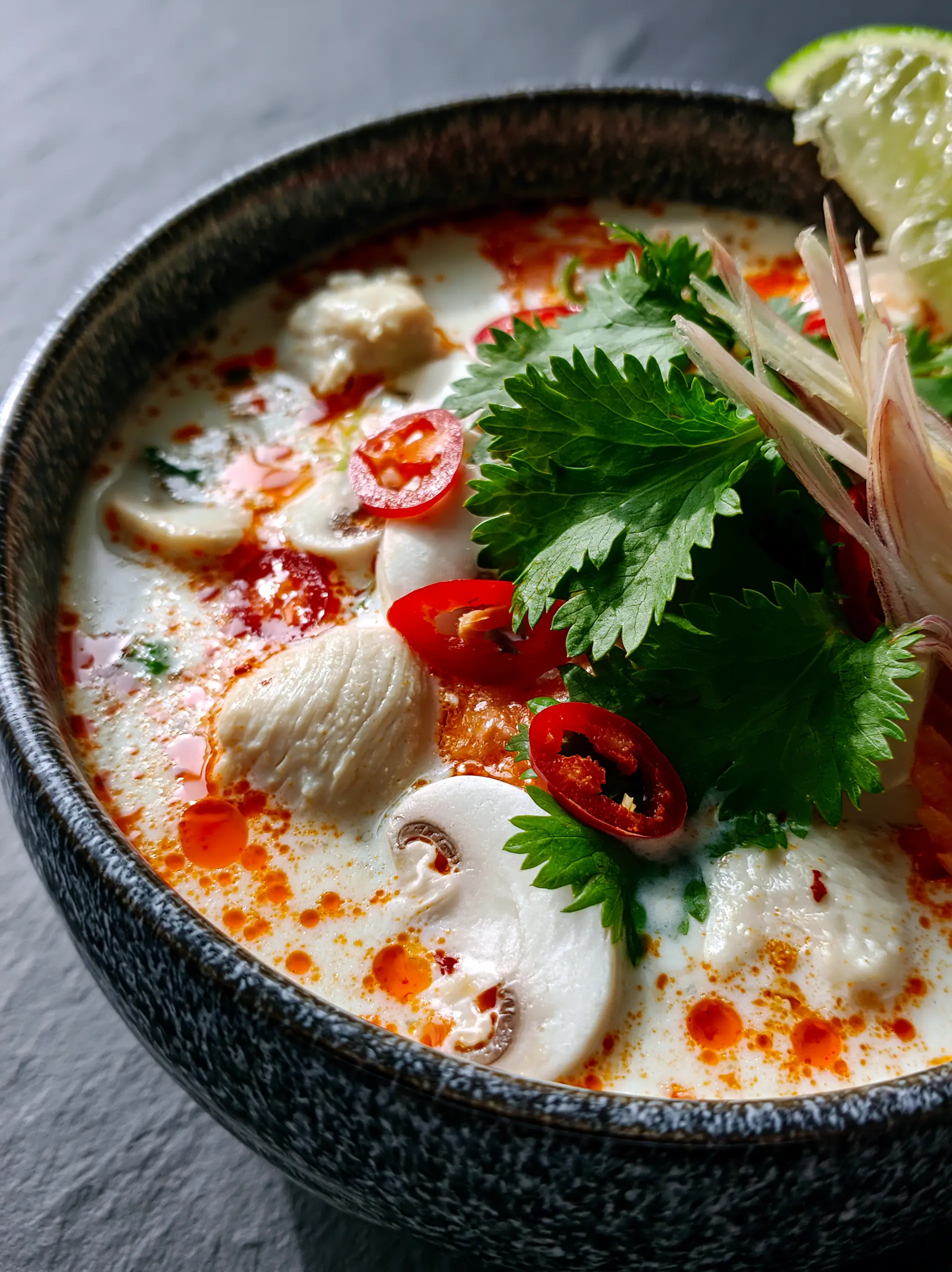 Macro photo showing the creamy white broth and shimmering orange chili oil of the Thai coconut chicken soup.