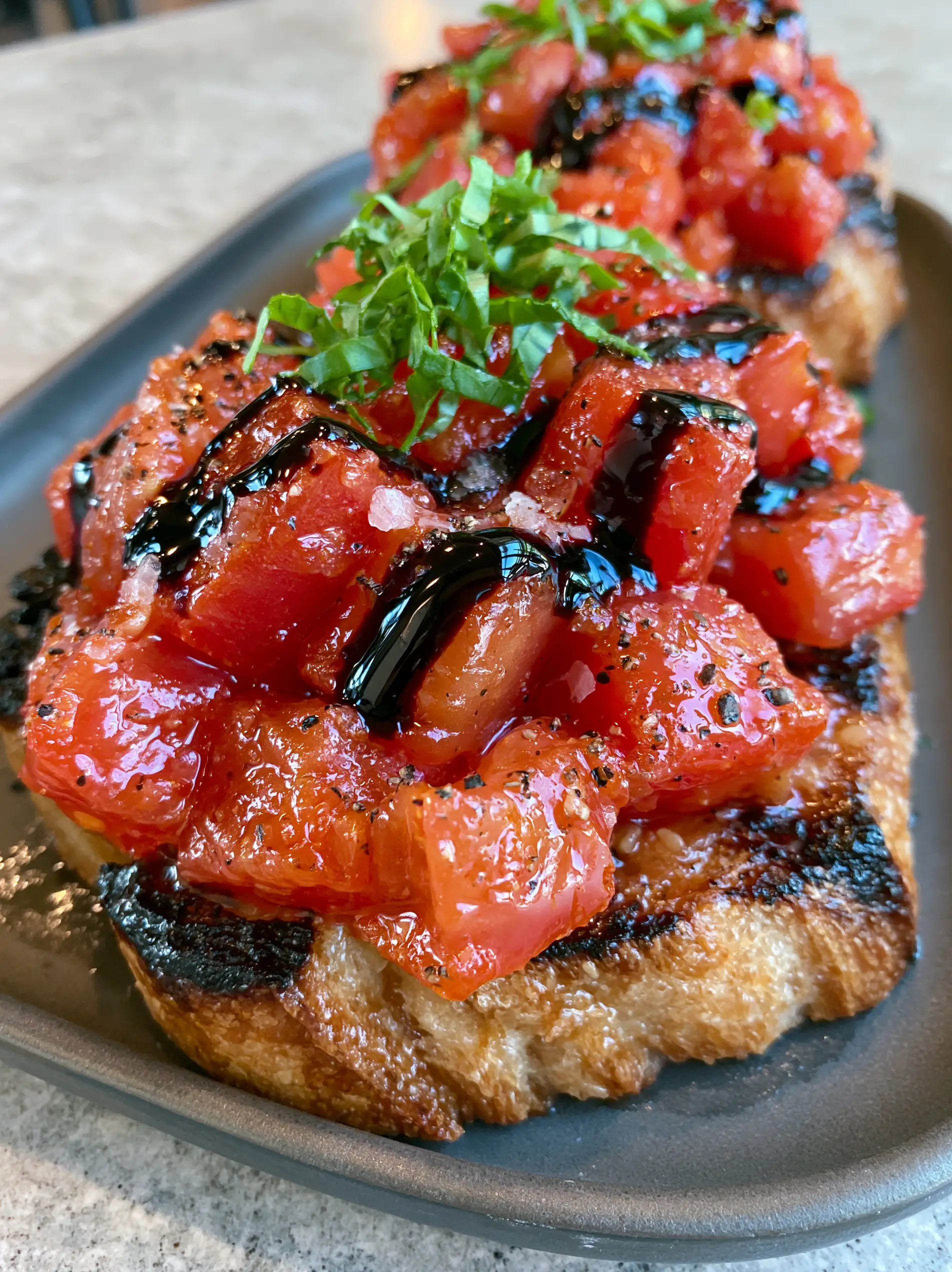 Handheld photo showing the glistening garlic-rubbed surface and charred edges of sourdough in this Bruschetta recipe. (Bruschetta recipe)