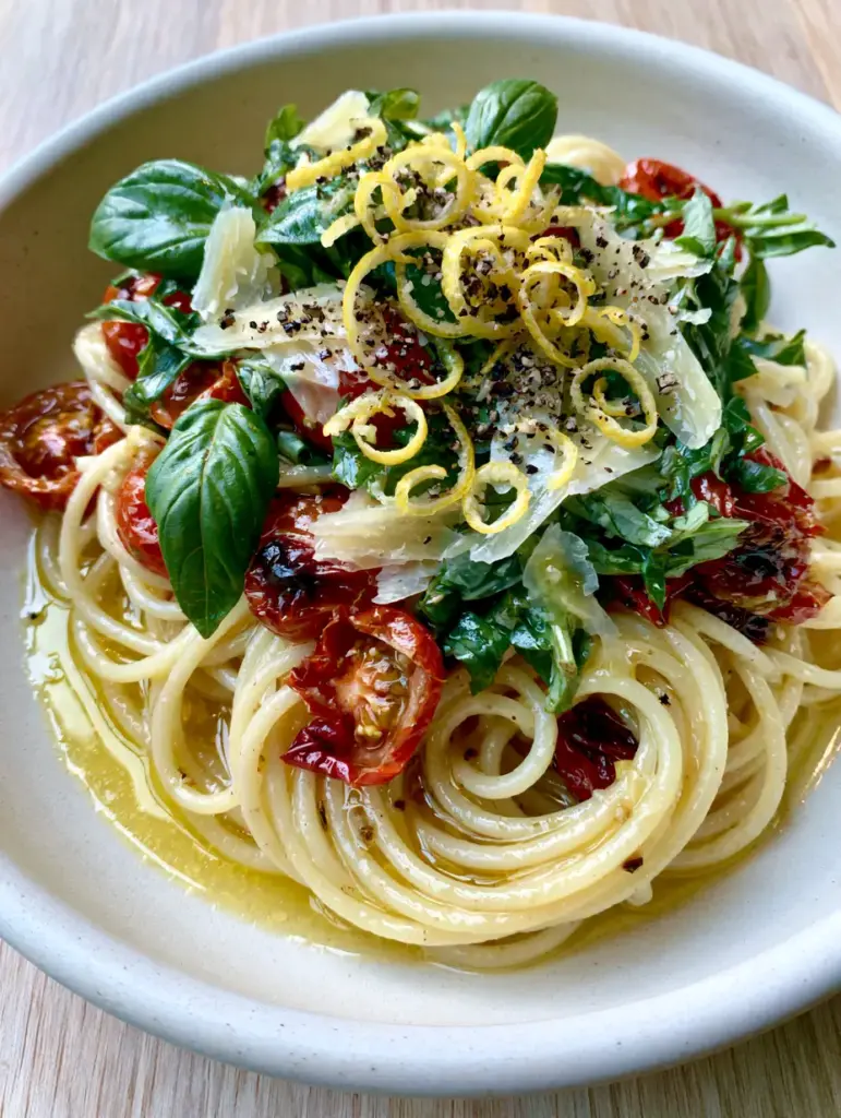 Handheld photo of summer pasta with vibrant green basil leaves and coarse black pepper.