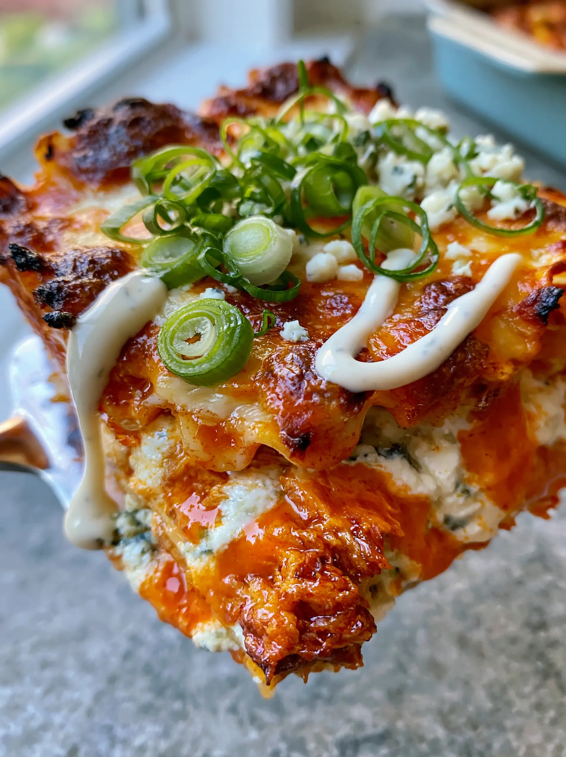 Extreme close-up of buffalo chicken lasagna layers with wavy noodles, orange sauce, and blue cheese crumbles. (buffalo chicken lasagna)