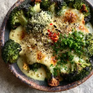 Extreme close-up of tender-crisp roasted broccoli florets with visible dark charred edges and glossy cheese sauce. (cheesy broccoli)
